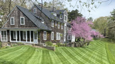 Freshly mowed lawn with diagonal cutting stripes in front of a large home surrounded by flowering spring trees